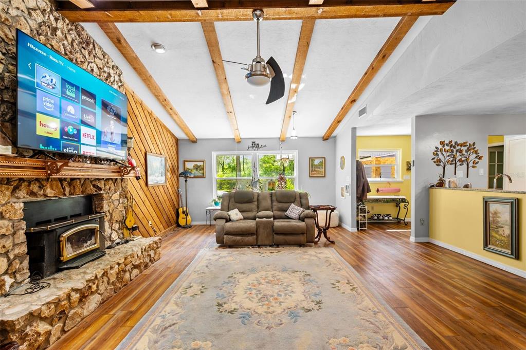 A living room features a stone fireplace, wood-paneled walls, exposed ceiling beams, and wood flooring — 16422 NE 10TH STREET, GAINESVILLE, FL