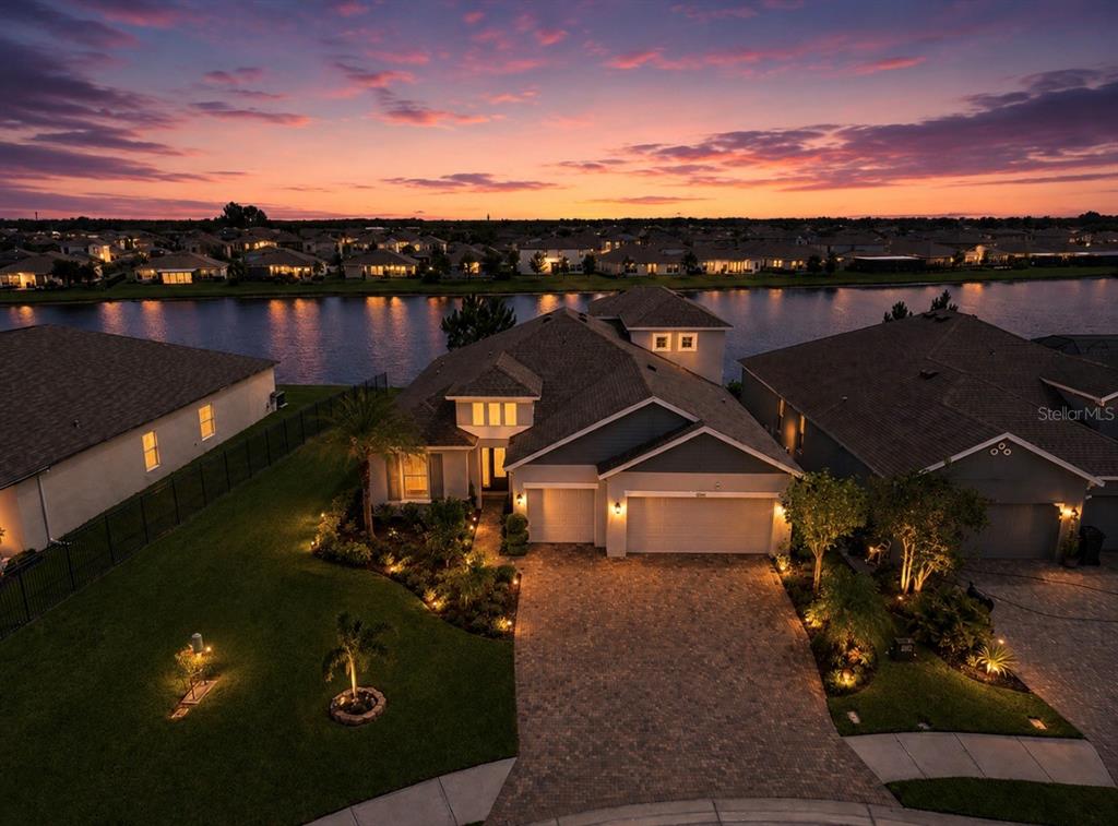 An aerial view shows a suburban house with a paved driveway at sunset by a lake — 5206 GAVELLA COVE, PALMETTO, FL