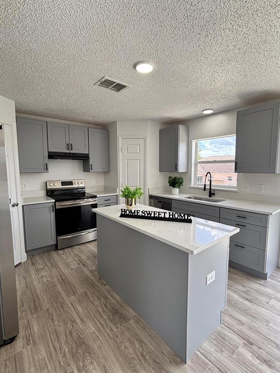 A kitchen features gray cabinets, white countertops, a center island, and wood-look tile flooring — 404 MANITOBA DRIVE, KISSIMMEE, FL
