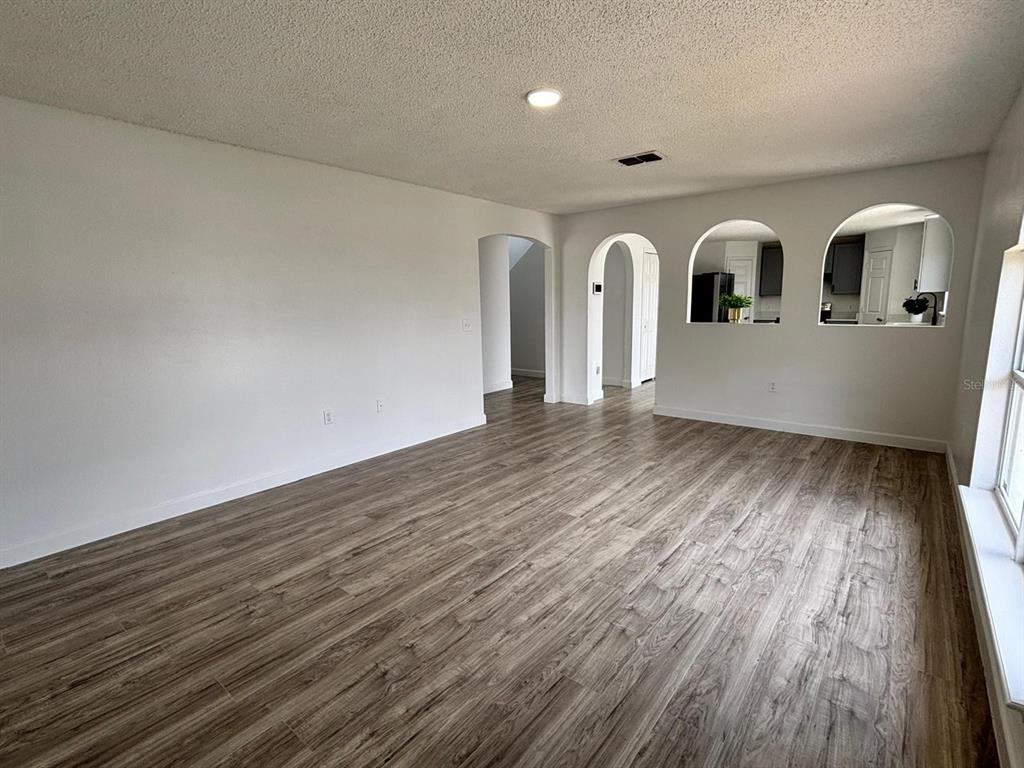 An empty living room features wood-look flooring, white walls, and arched cutouts into the kitchen — 404 MANITOBA DRIVE, KISSIMMEE, FL
