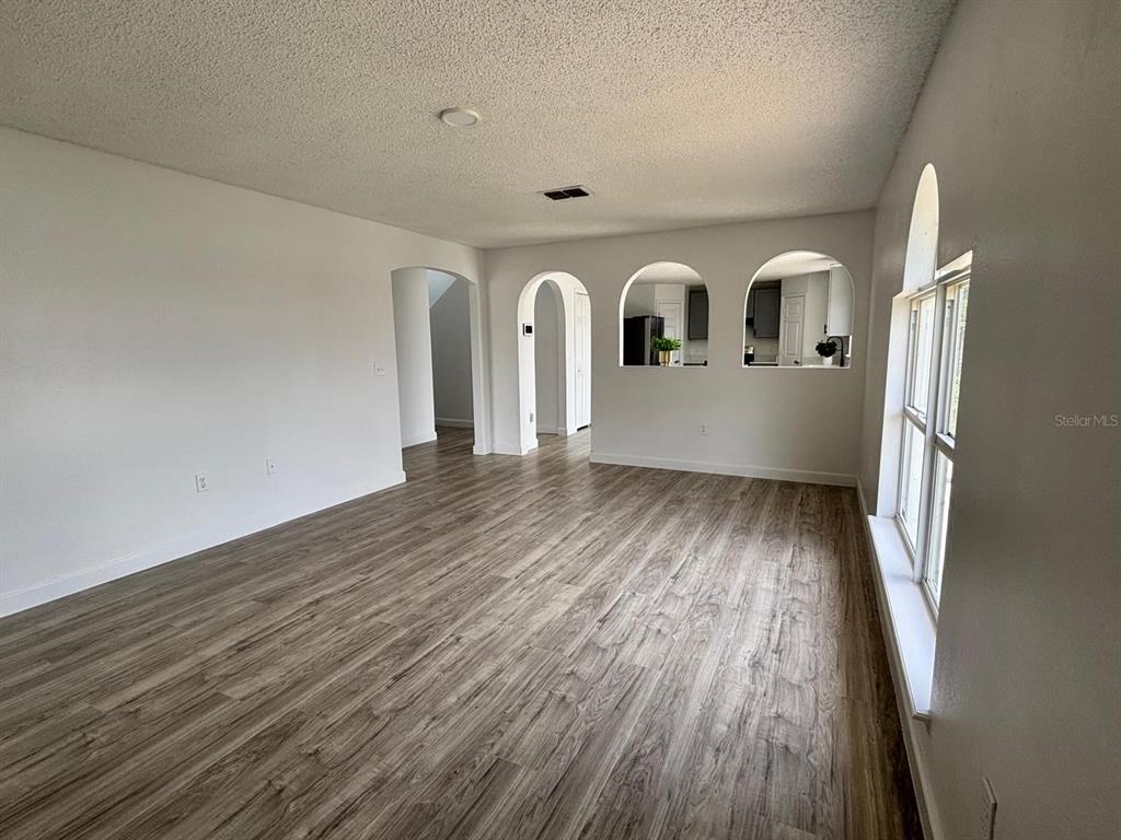 An empty living room features wood-look flooring, white walls, and arched cutouts into the kitchen — 404 MANITOBA DRIVE, KISSIMMEE, FL