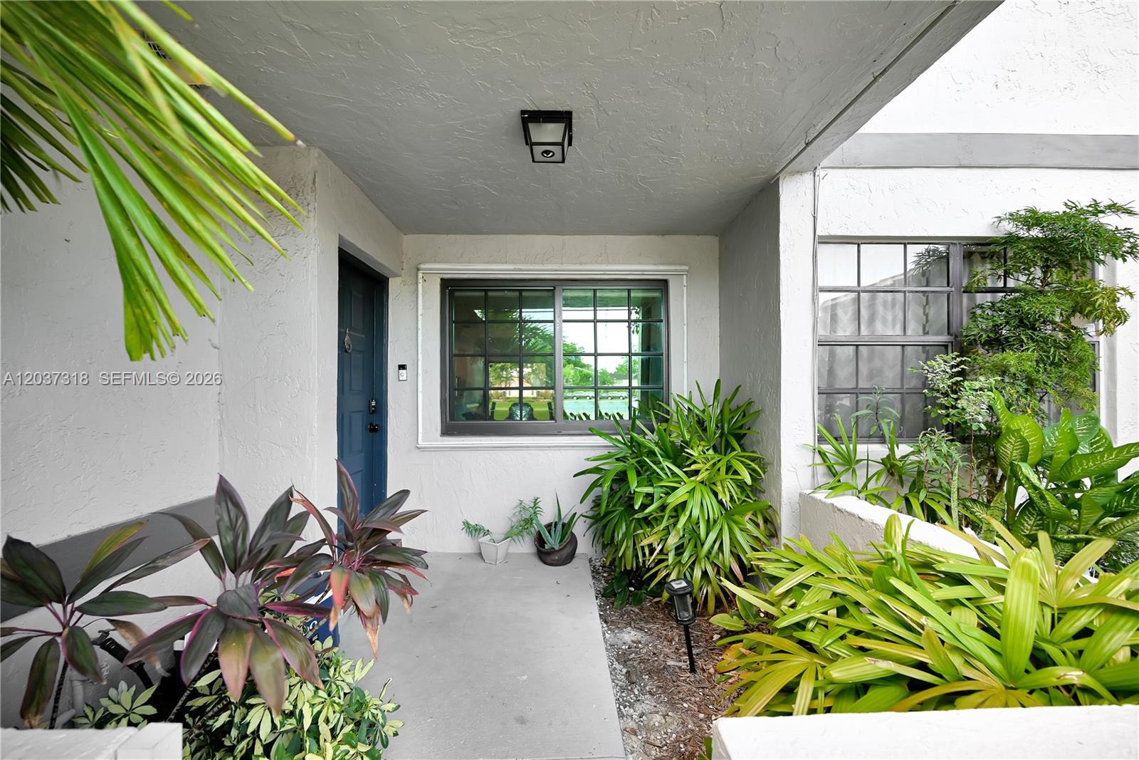 A covered entryway features a dark blue door, a window with a grid, and potted plants — 15561 SW 110th Ter, Miami FL 33196, MIAMI, FL