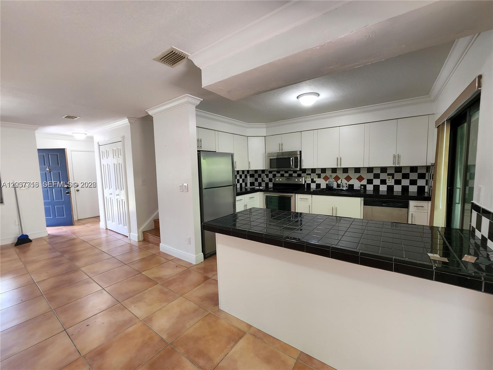 A kitchen features white cabinets, black tile countertops, and a checkered backsplash — 15561 SW 110th Ter, Miami FL 33196, MIAMI, FL