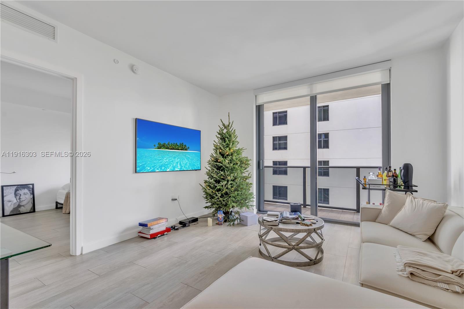 A living room features a wall-mounted television, a Christmas tree, and a balcony view — 55 SW 9th St # 2610, Miami FL 33130, MIAMI, FL