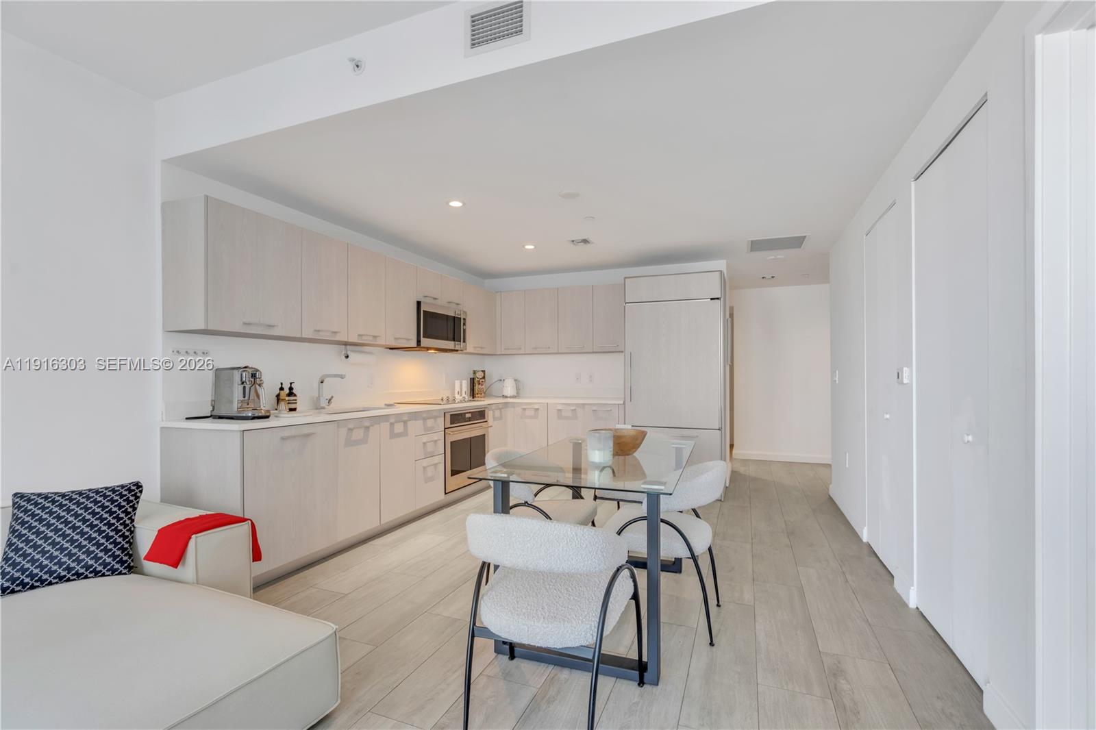 A modern kitchen features light wood cabinetry, stainless steel appliances, and a glass dining table — 55 SW 9th St # 2610, Miami FL 33130, MIAMI, FL