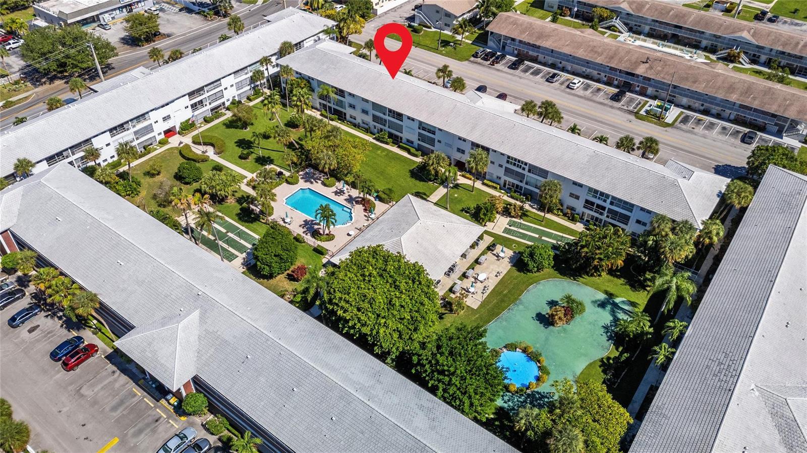 An aerial view shows apartment buildings surrounding a courtyard with a pool and pond — 2050 NE 39th Street # 302e, Lighthouse Point FL 33064, LIGHTHOUSE POINT, FL