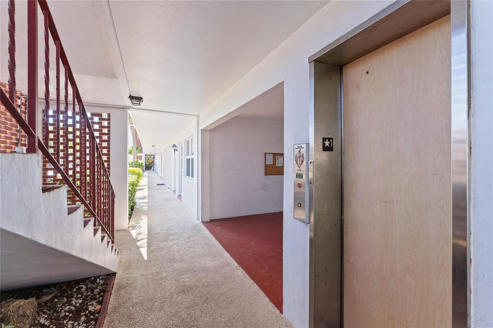 An outdoor hallway features a staircase with a red railing and an elevator door — 2050 NE 39th Street # 302e, Lighthouse Point FL 33064, LIGHTHOUSE POINT, FL