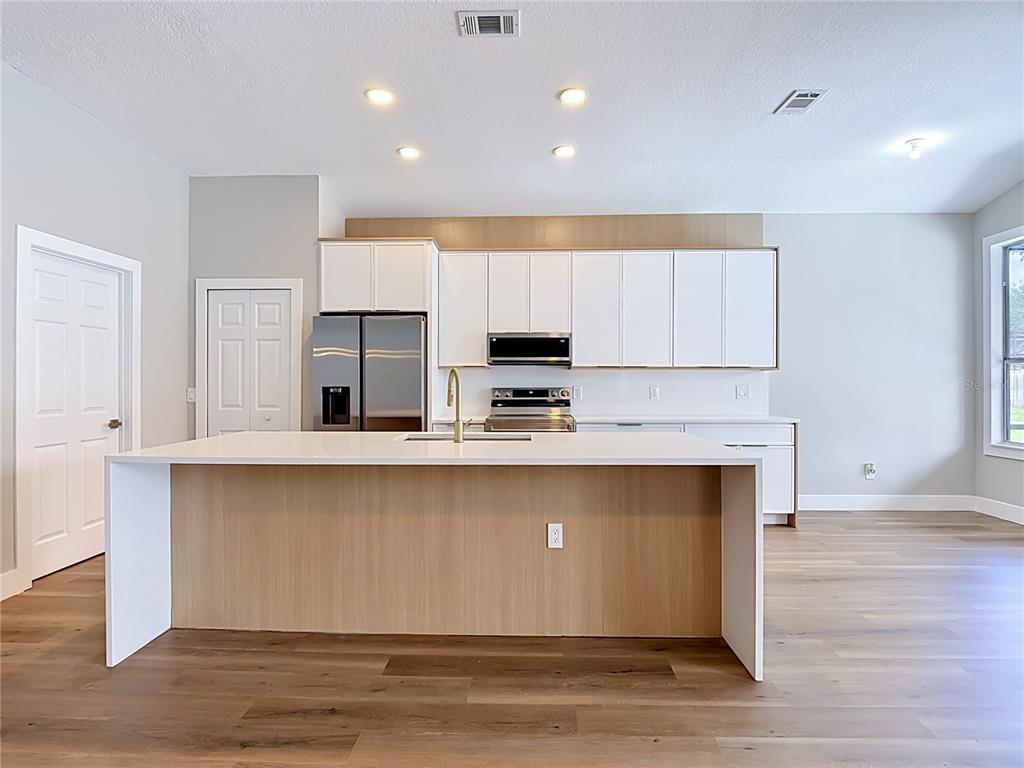 A modern kitchen features white cabinets, a wood-paneled island, and stainless steel appliances — 5013 TERRA VISTA WAY, ORLANDO, FL