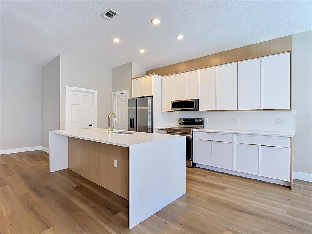 A modern kitchen features white cabinets, a waterfall island, and light wood flooring — 5013 TERRA VISTA WAY, ORLANDO, FL