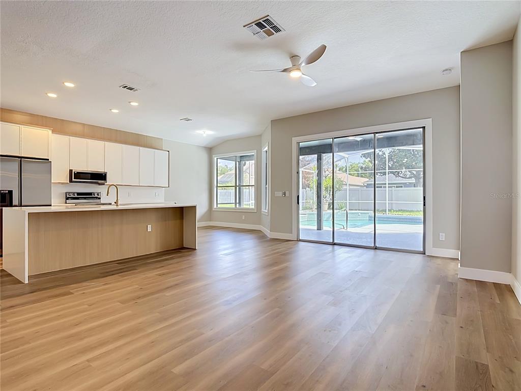 A modern open-concept kitchen and living area with light wood flooring and a backyard pool — 5013 TERRA VISTA WAY, ORLANDO, FL