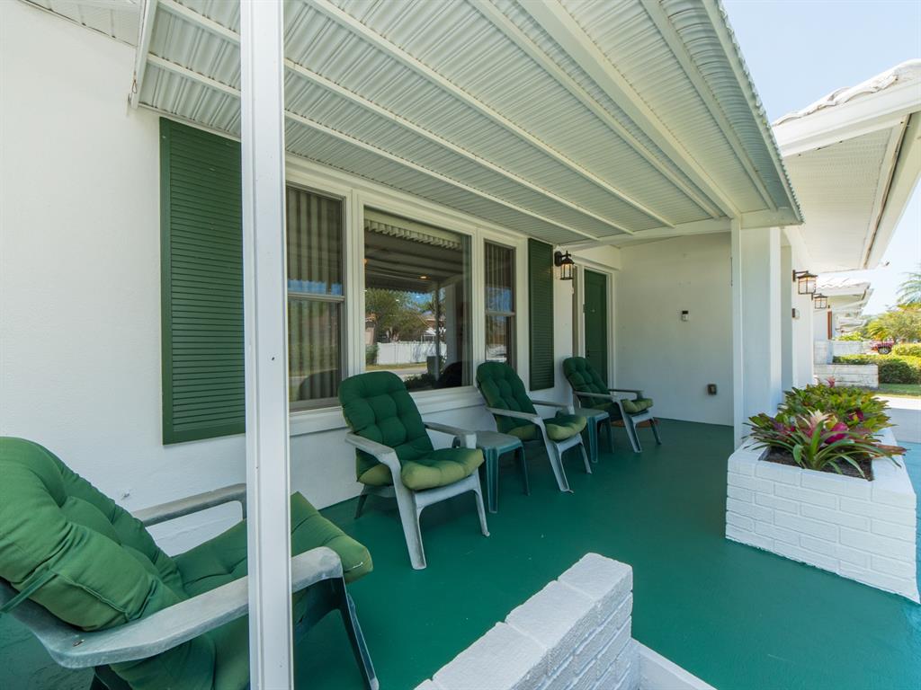 A covered patio features green flooring, white brick planters, and several chairs with green cushions — 9227 143RD STREET, SEMINOLE, FL