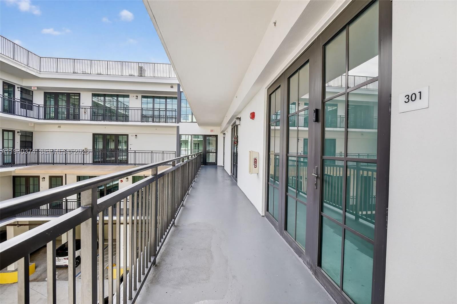 An outdoor walkway with metal railings leads past glass-paned doors of a multi-story apartment building — 4100 SW 64th Ave # 301, Davie FL 33314, DAVIE, FL