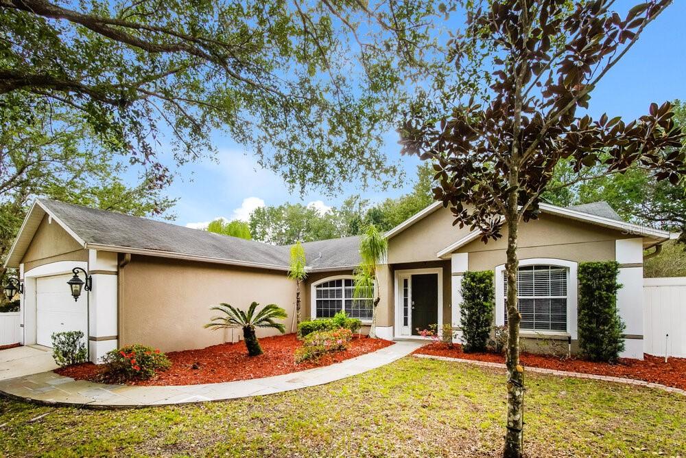 A single-story house with a tan stucco exterior, a garage, and a landscaped front yard — 605 CHERRY LAUREL STREET, MINNEOLA, FL