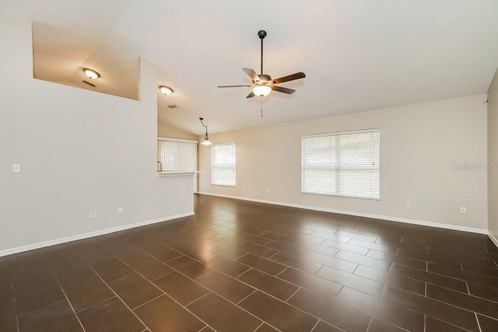 An empty living room features dark tile flooring, light walls, and a ceiling fan — 605 CHERRY LAUREL STREET, MINNEOLA, FL
