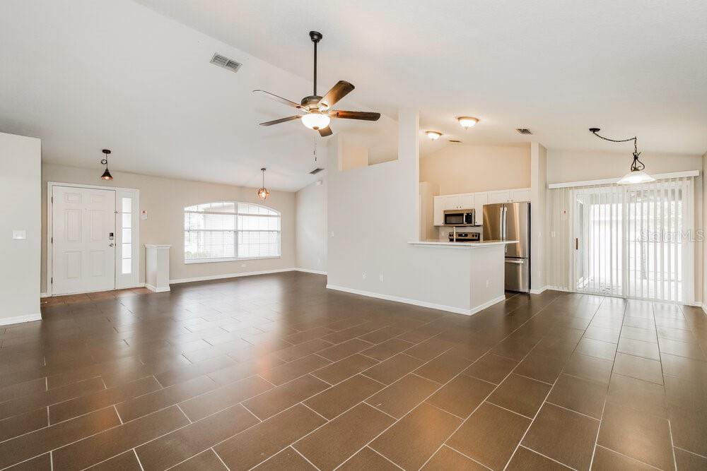 An open-concept living and dining area features dark tile flooring and a kitchen with stainless appliances — 605 CHERRY LAUREL STREET, MINNEOLA, FL