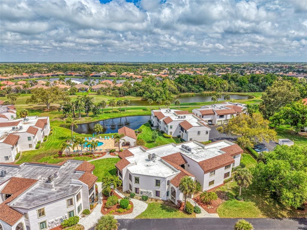 An aerial view shows multi-story apartment buildings, a swimming pool, and a pond with landscaping — 796 CAPRI ISLES BOULEVARD UNIT 130, VENICE, FL