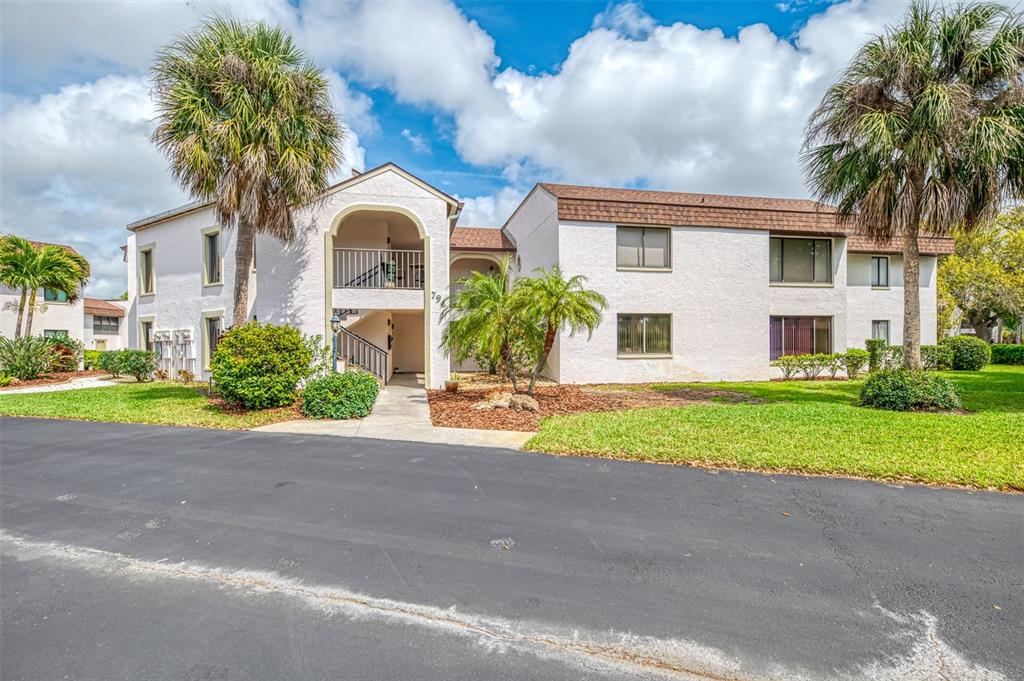 A two-story apartment building with a stucco exterior, palm trees, and a paved driveway — 796 CAPRI ISLES BOULEVARD UNIT 130, VENICE, FL