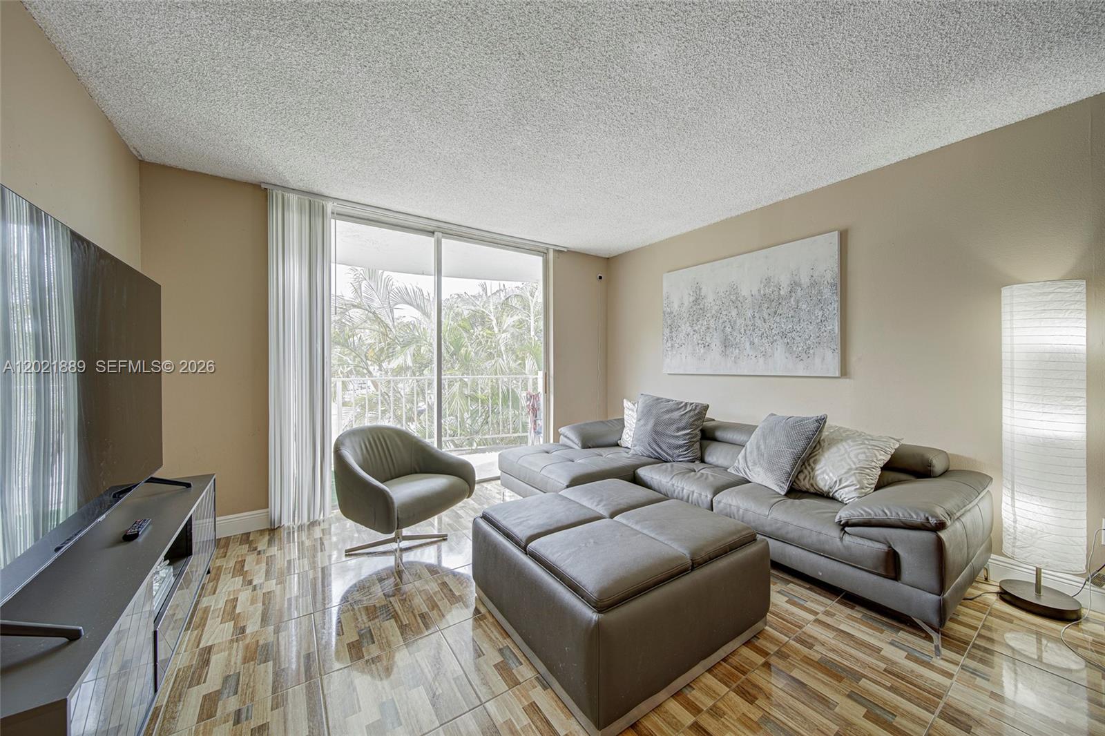 A living room features a gray sectional sofa, a swivel chair, and patterned tile flooring — 494 NW 165th St Rd # 205, Miami FL 33169, MIAMI, FL