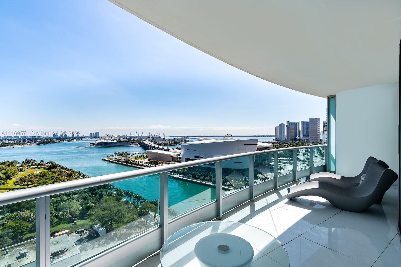 A balcony with two lounge chairs overlooks a bay, a bridge, and a city skyline — 900 Biscayne Blvd # 2006, Miami FL 33132, MIAMI, FL