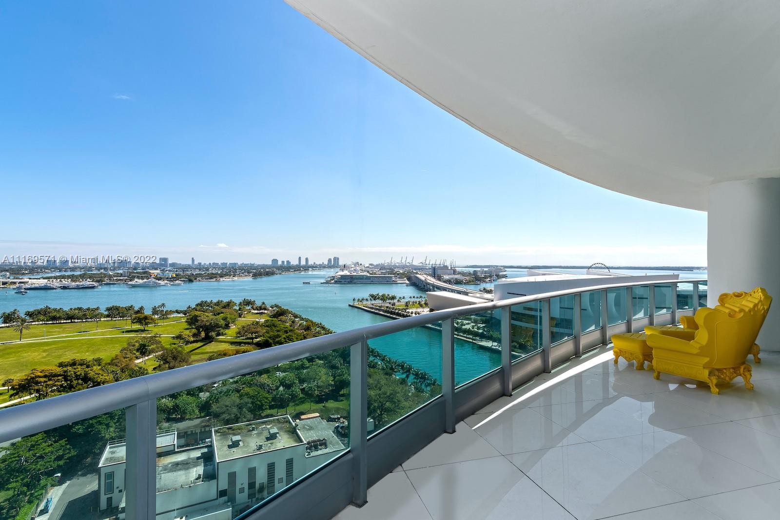 A high-rise balcony features white tile flooring, a glass railing, and a yellow armchair — 900 Biscayne Blvd # 2006, Miami FL 33132, MIAMI, FL