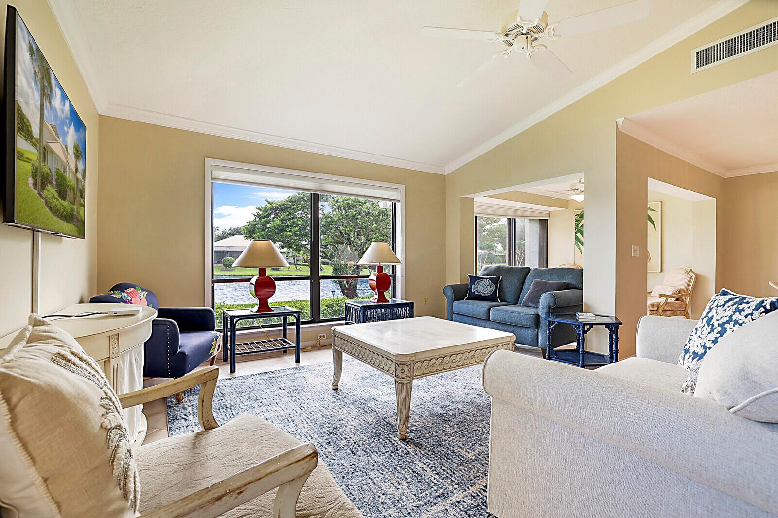 A living room features a blue sofa, white armchair, coffee table, and large windows overlooking water — 5611 SE Foxcross Place # 5611, Stuart FL 34997, STUART, FL