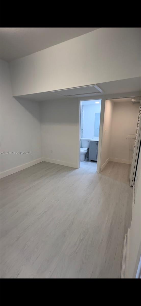 A bedroom with light wood-look flooring leads to an attached bathroom and a walk-in closet — HOMESTEAD, FL