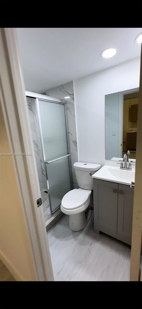 A small bathroom features a gray vanity, a white toilet, and a glass-enclosed shower — HOMESTEAD, FL