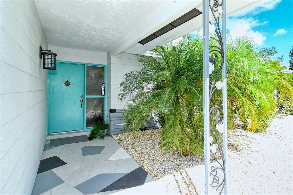A turquoise front door with a side window sits on a patterned patio near palm trees — 6758 S LOCKWOOD RIDGE ROAD, SARASOTA, FL