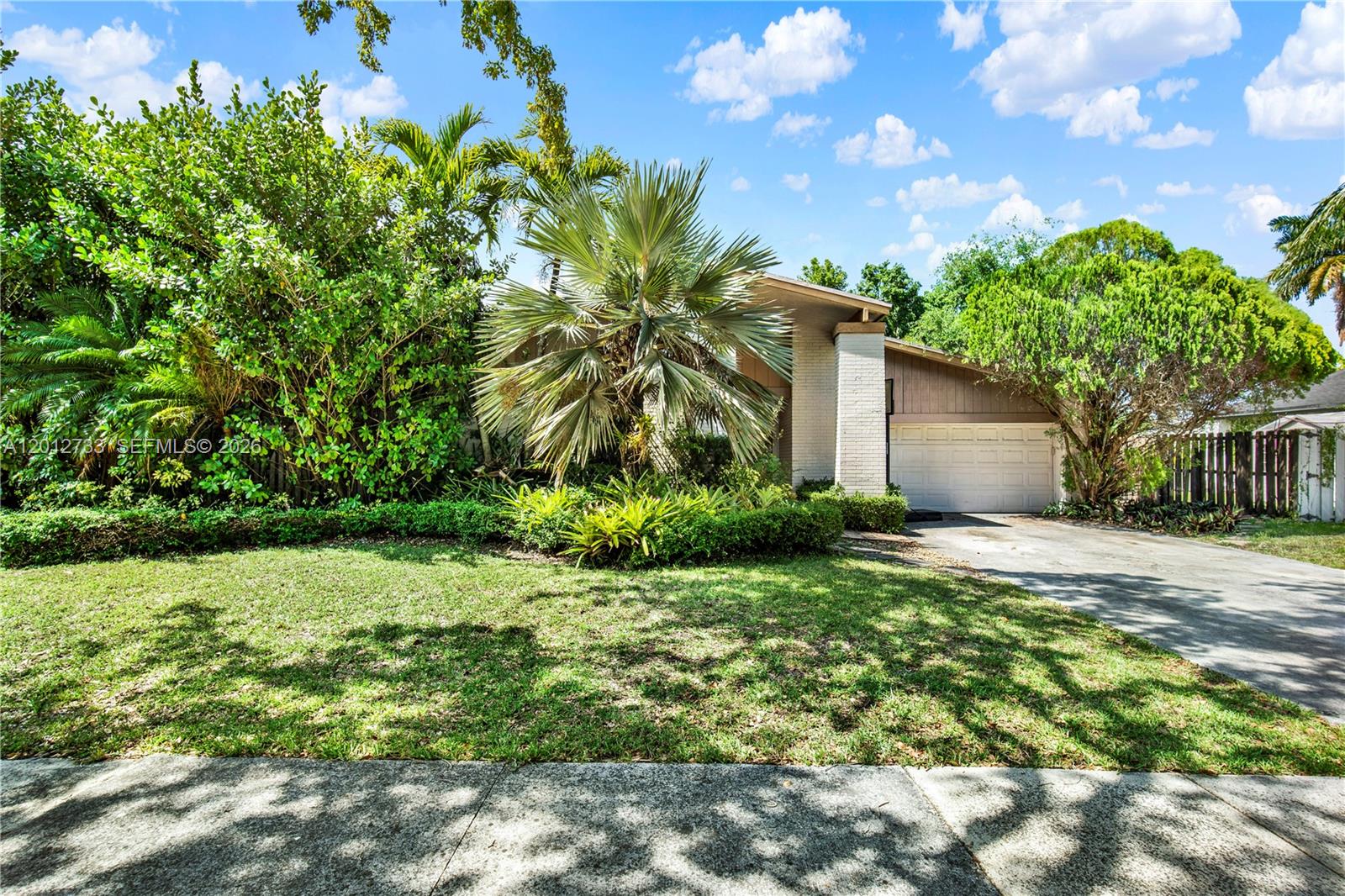 A single-story house with a white brick facade, a garage, and lush landscaping — 13455 SW 104th Ter, Miami FL 33186, MIAMI, FL