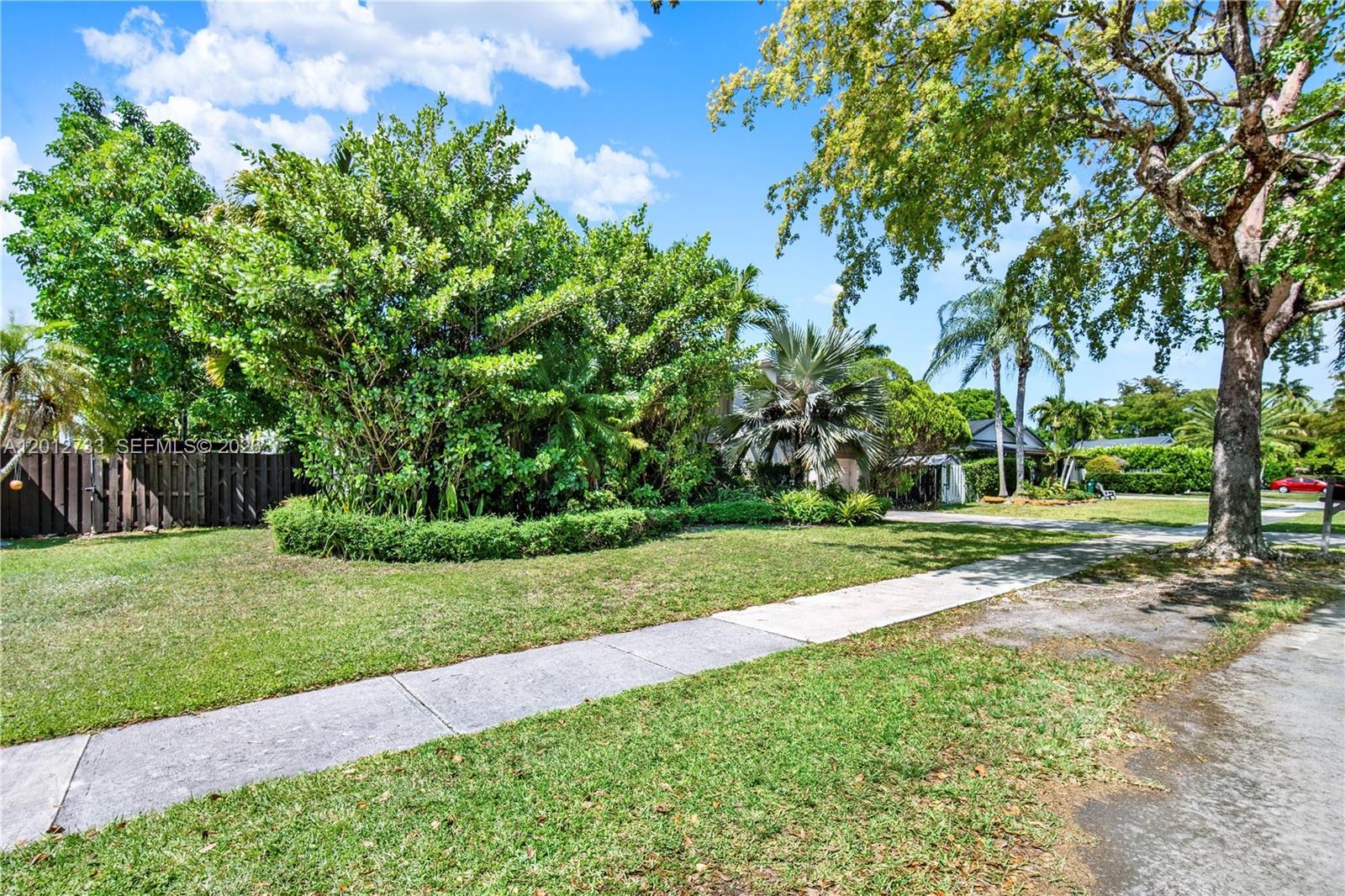 A grassy front yard features a concrete sidewalk, mature trees, and dense landscaping — 13455 SW 104th Ter, Miami FL 33186, MIAMI, FL