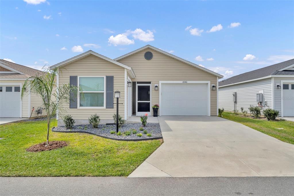A single-story house with beige vinyl siding, a front-facing garage, and a landscaped front yard — 1640 OLIVIA TERRACE, THE VILLAGES, FL