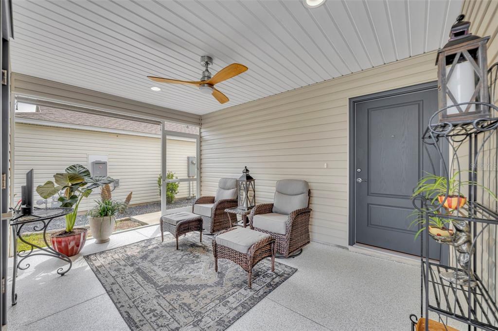 A covered patio features wicker chairs, ottomans, a ceiling fan, and a dark gray door — 1640 OLIVIA TERRACE, THE VILLAGES, FL