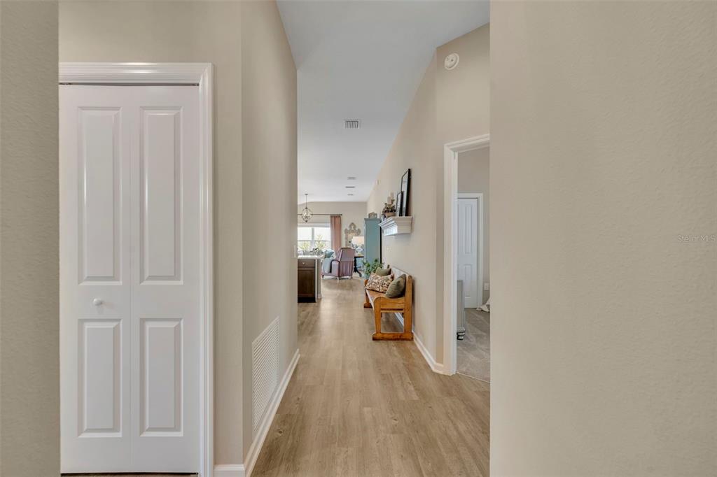 A hallway with light wood-look flooring leads to an open-concept living area and kitchen — 1640 OLIVIA TERRACE, THE VILLAGES, FL