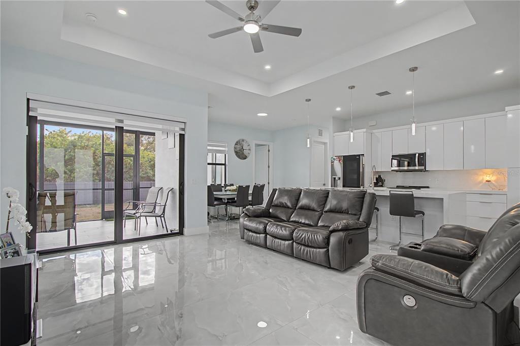 An open-concept living room and kitchen feature glossy tile floors, white cabinetry, and sliding doors — 3705 23RD STREET SW, LEHIGH ACRES, FL