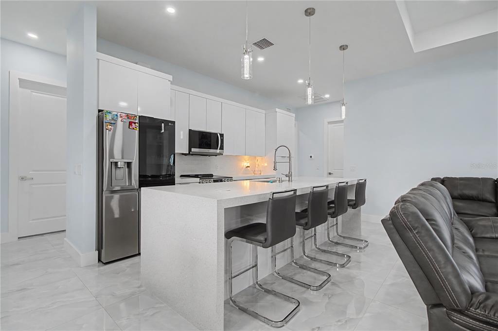 A modern kitchen features white cabinetry, a large quartz island with bar seating, and tile flooring — 3705 23RD STREET SW, LEHIGH ACRES, FL