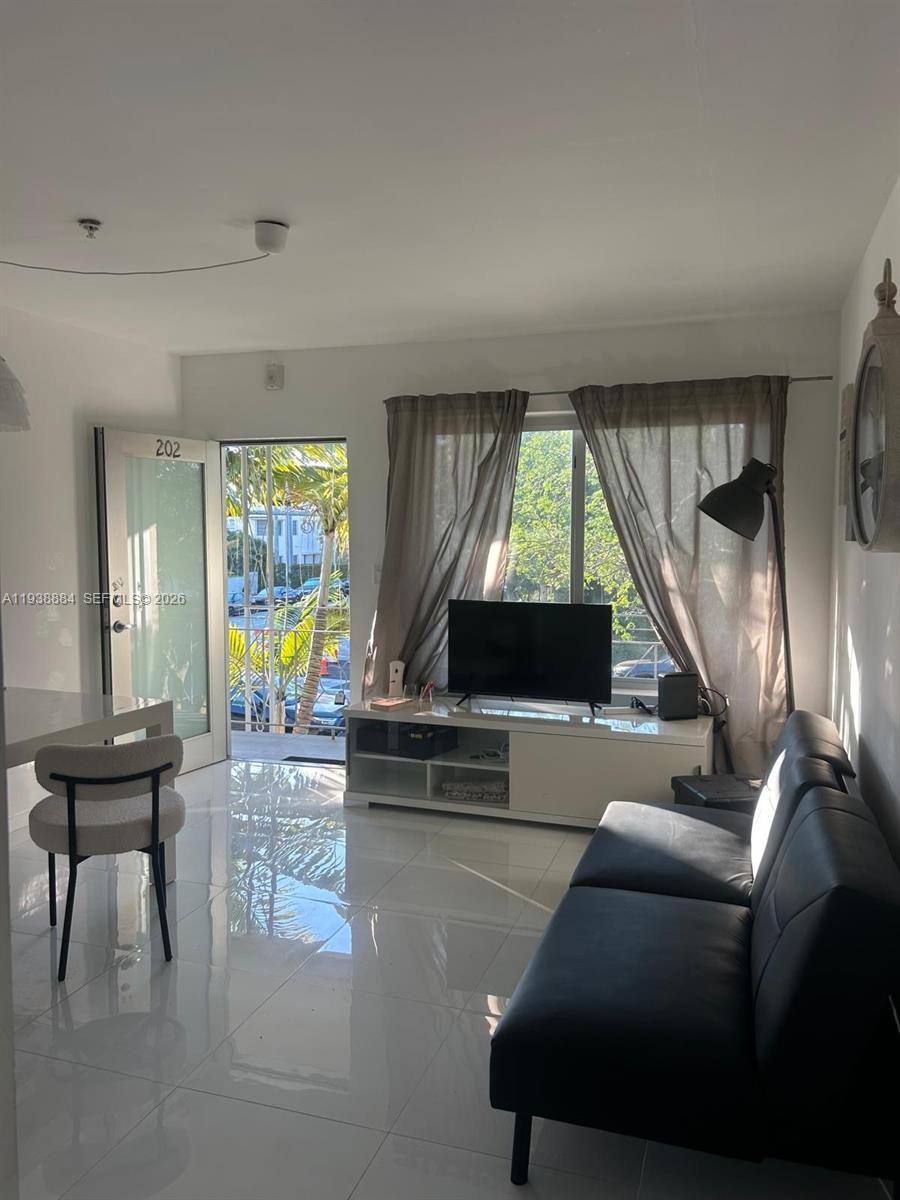 A living room features white tile floors, a black sofa, a television, and a balcony door — 801 15th St # 202, Miami Beach FL 33139, MIAMI BEACH, FL