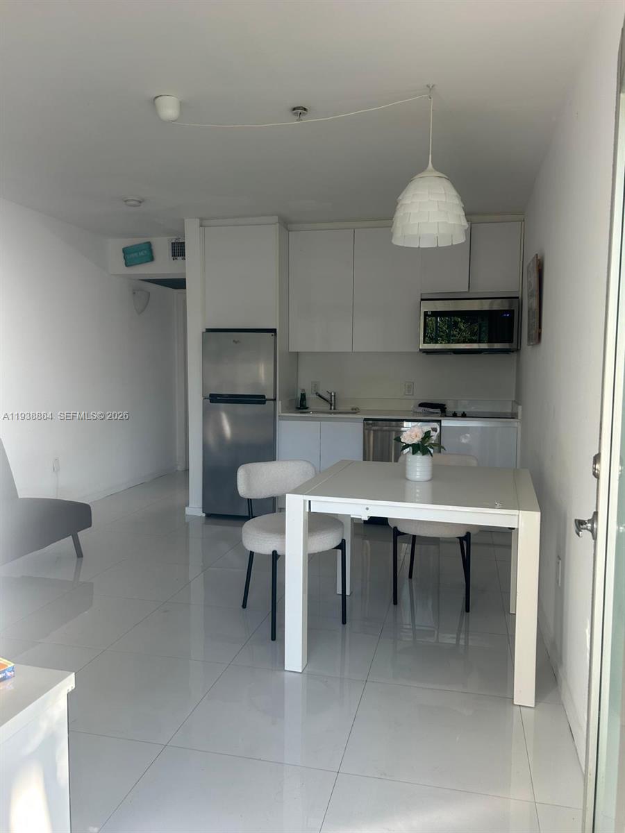 A small kitchen with white cabinets and stainless steel appliances sits beside a dining area — 801 15th St # 202, Miami Beach FL 33139, MIAMI BEACH, FL