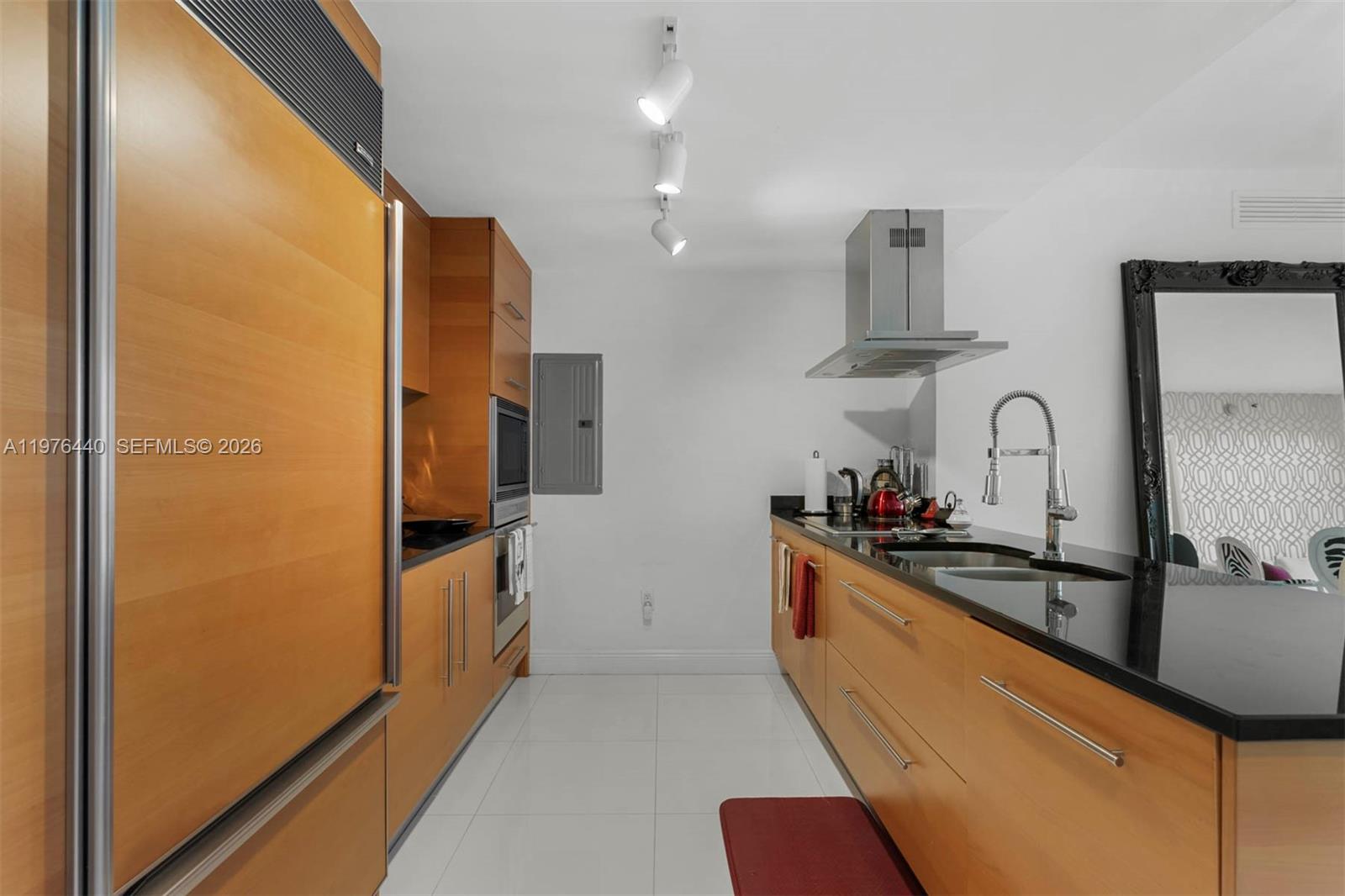 A galley kitchen features wood cabinetry, black countertops, stainless steel appliances, and white tile flooring — 495 Brickell Ave # 805, Miami FL 33131, MIAMI, FL