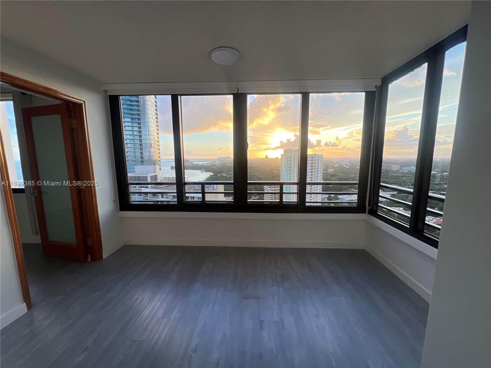 An empty room with gray wood-look flooring and floor-to-ceiling windows overlooking a city skyline — 2333 Brickell Ave, Miami FL 33129, MIAMI, FL