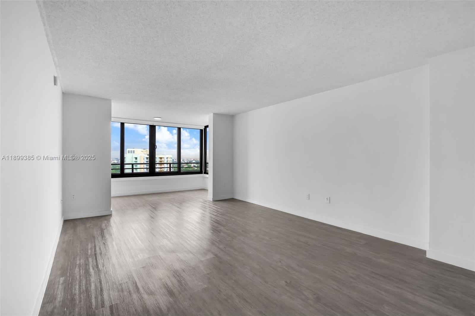An empty room features white walls, gray wood-look flooring, and large windows with city views — 2333 Brickell Ave, Miami FL 33129, MIAMI, FL