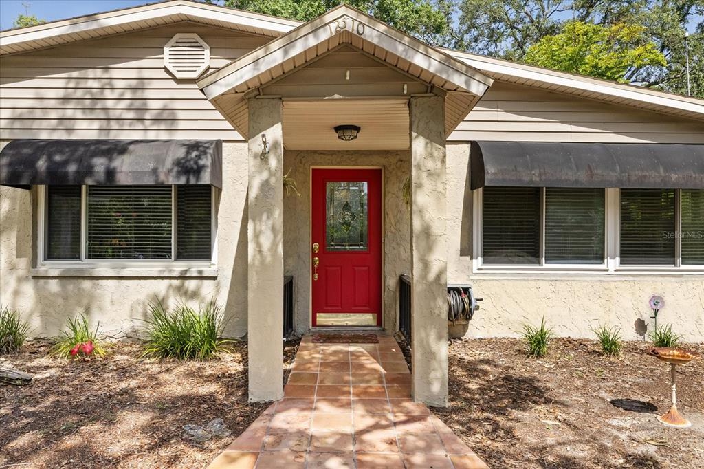 A front exterior view of a house with a red door and a tiled walkway — 12510 NOREAST LAKE DRIVE, TAMPA, FL