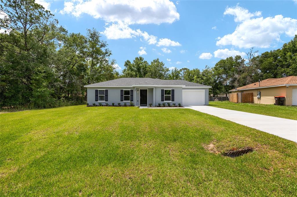 A single-story gray house with a white garage and a large front lawn — 94 DOGWOOD DRIVE LOOP, OCALA, FL