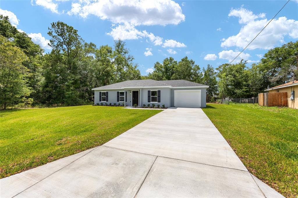 A single-story gray house with a white garage and a concrete driveway sits on grass — 94 DOGWOOD DRIVE LOOP, OCALA, FL