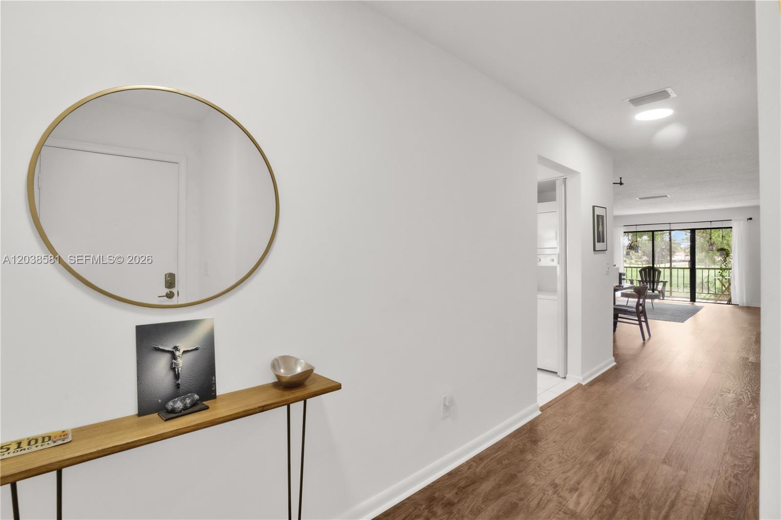 A hallway with wood-look flooring leads to a living area with a sliding glass door — 21650 Juego Cir # 24H, Boca Raton FL 33433, BOCA RATON, FL