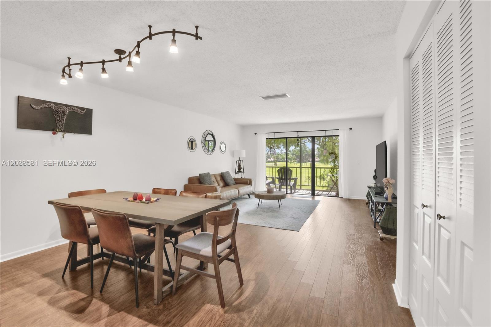 An open-concept living and dining area features wood-look flooring, a track light, and balcony access — 21650 Juego Cir # 24H, Boca Raton FL 33433, BOCA RATON, FL