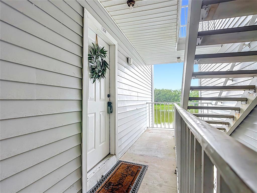 An exterior view of an apartment entrance with a white door, wreath, and metal staircase — 1229 BERMUDA LAKES LANE UNIT 206, KISSIMMEE, FL