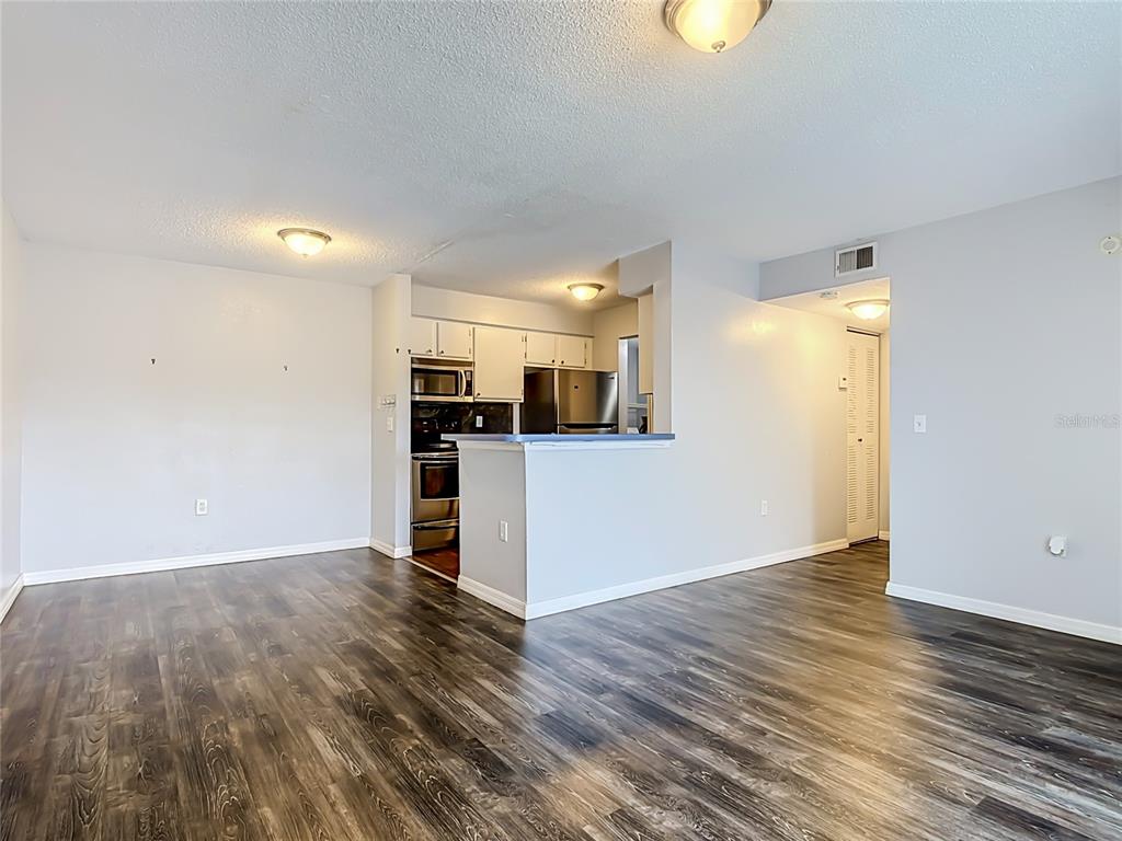 An open-concept living area features wood-look flooring, light gray walls, and a kitchen with stainless appliances — 1229 BERMUDA LAKES LANE UNIT 206, KISSIMMEE, FL