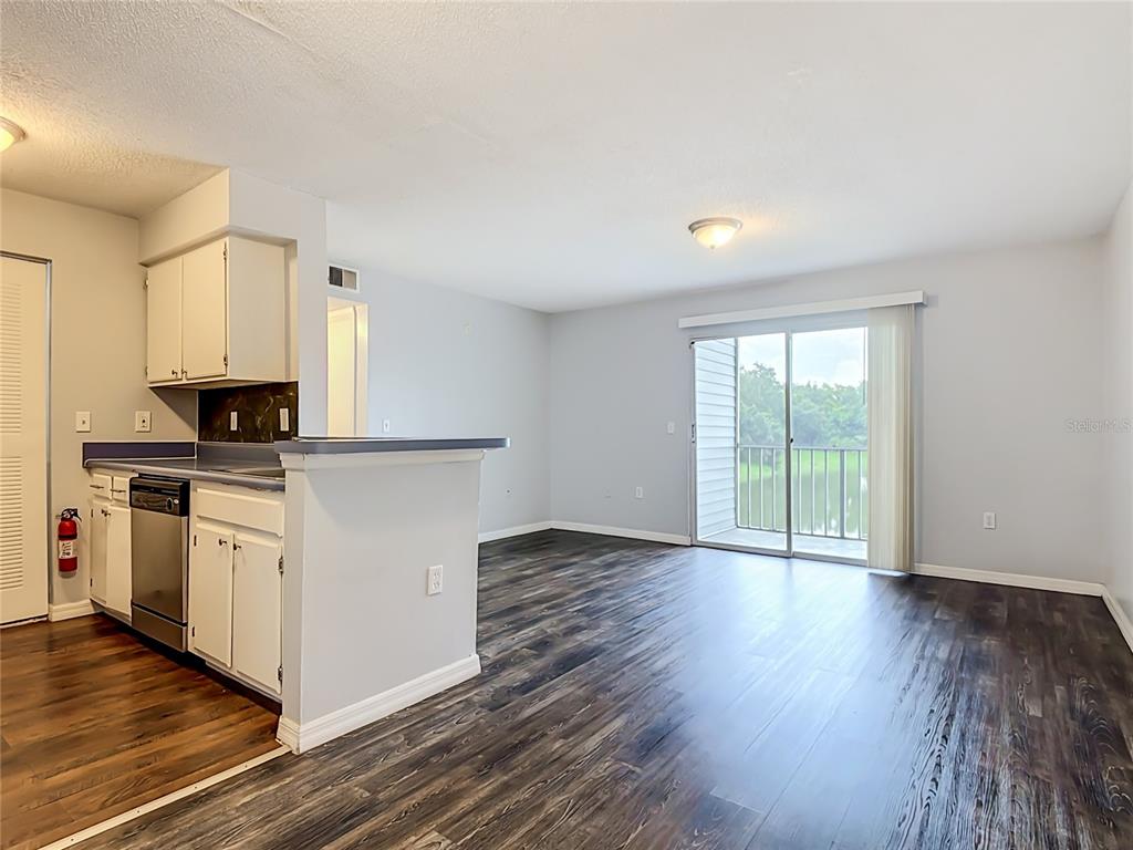 An open-concept kitchen and living area features dark wood-look flooring and a sliding glass door — 1229 BERMUDA LAKES LANE UNIT 206, KISSIMMEE, FL