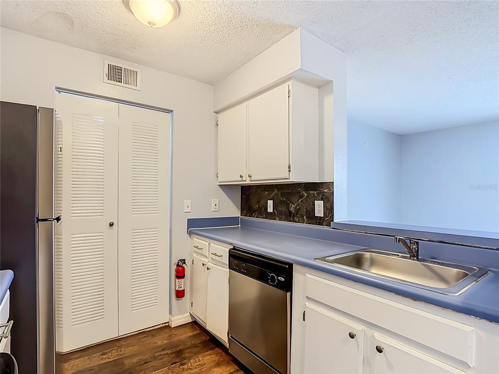 A kitchen features white cabinets, blue countertops, a stainless steel dishwasher, and a pantry closet — 1229 BERMUDA LAKES LANE UNIT 206, KISSIMMEE, FL