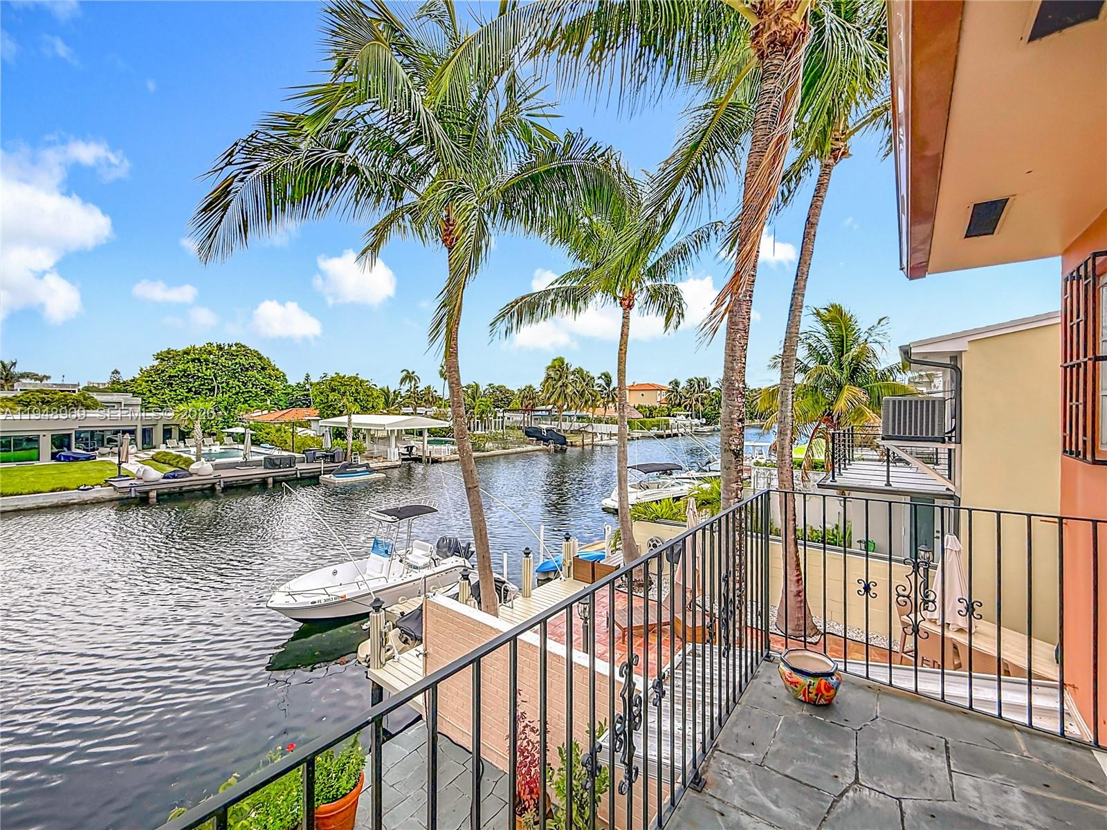 A balcony with stone flooring overlooks a canal with docked boats and palm trees — 2205 NE 123rd St, North Miami FL 33181, NORTH MIAMI, FL